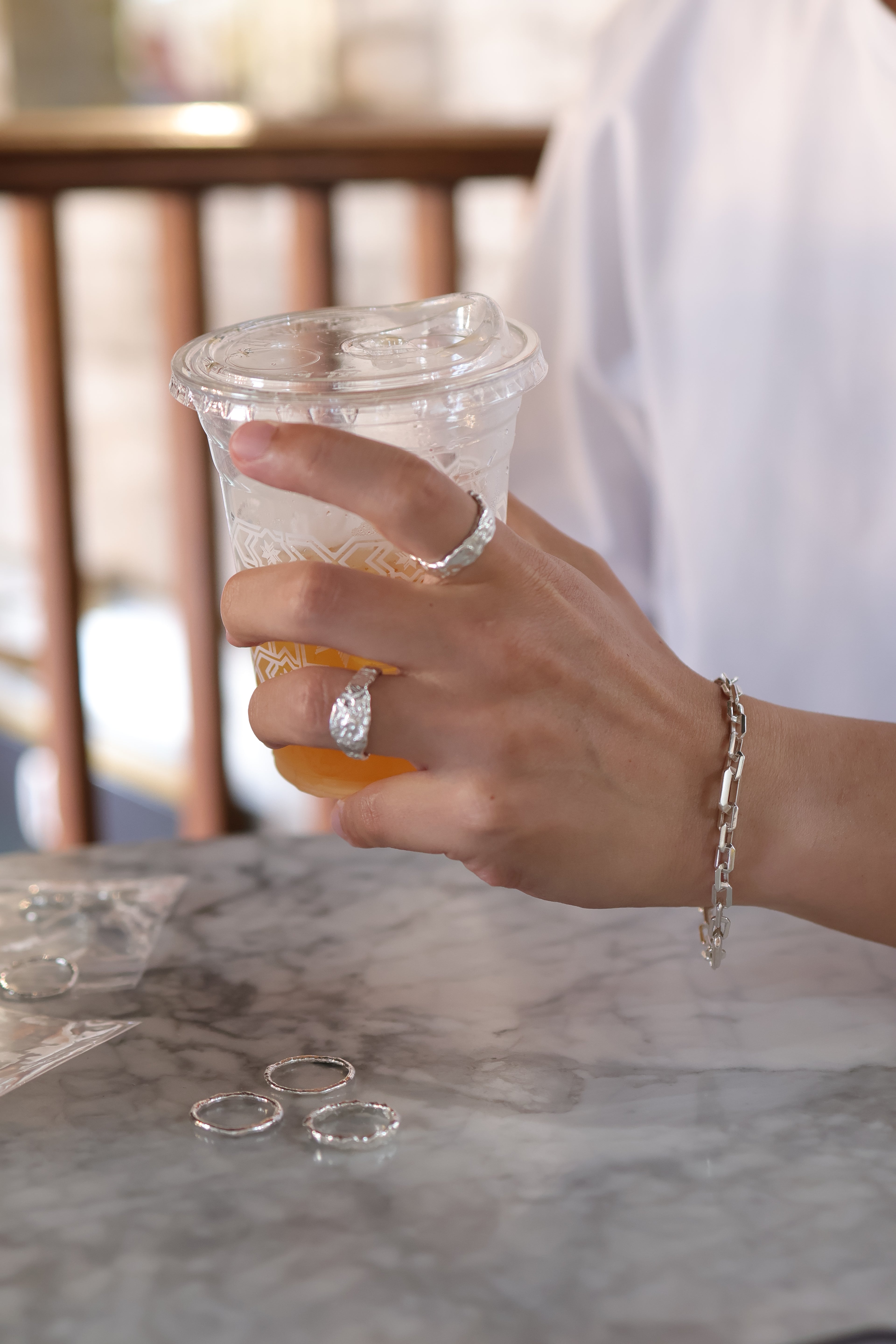 Molten silver rings and a chain bracelet worn at a marble café table